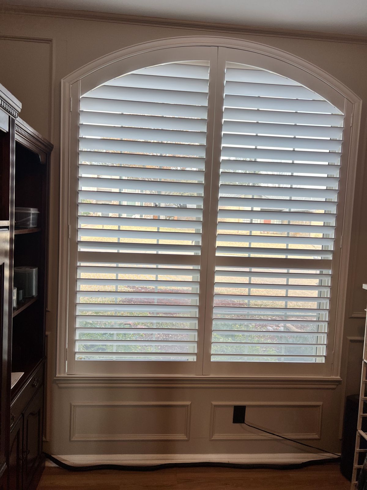 Arched white plantation shutters installed on a tall window