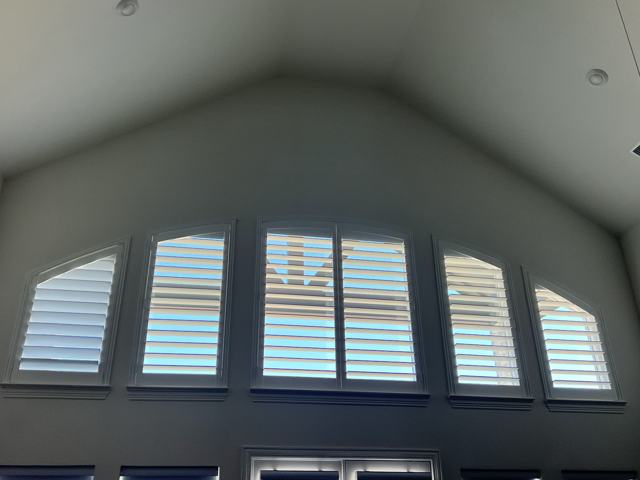 Plantation shutters on a row of arched vaulted-ceiling windows